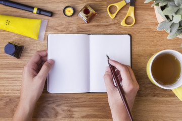 Mano con pluma escribiendo en libreta en blanco y objetos amarillos
