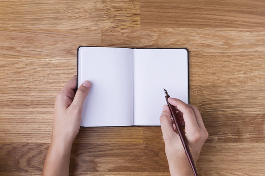 Mano con pluma escribiendo en libreta en blanco