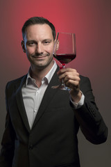 man tasting red wine in jacket in front of red background