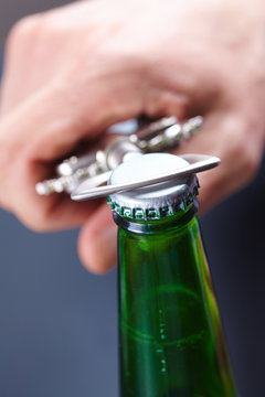 A hand opening a bottle of beer