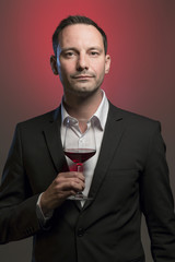man tasting red wine in jacket in front of red background