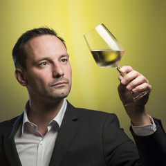 man tasting white wine in jacket in front of yellow background