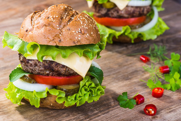 Big hamburger with beef cutlet and vegetables on wood plate