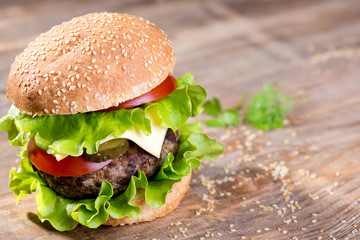 Big hamburger with beef cutlet and vegetables on wood plate