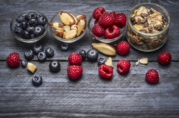 Glass bowls with ingredients for healthy breakfast - muesli,berries and nuts on blue rustic wooden background