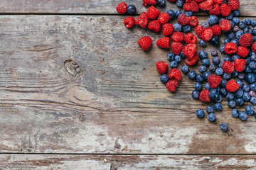 Top view. On an antique wooden table and worn from the sun and bad weather sit some raspberries and blueberries arranged randomly after being caught