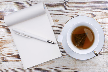 Tea and opened notebook on a wooden background.