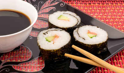 Sushi on a black plate on a red mat with chopsticks