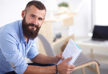 Young businessman sitting on chair with book in office