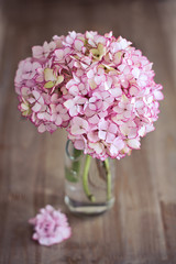Pink hydrangea flowers in a glass vase on a wooden table. 