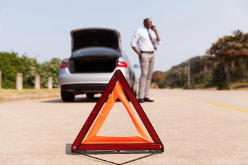 african male driver calling for help after car broke-down