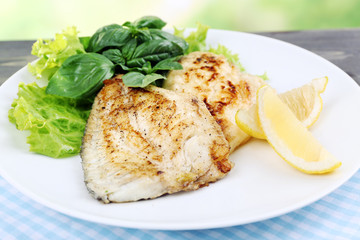 Dish of fish fillet with greens and lemon on table close up