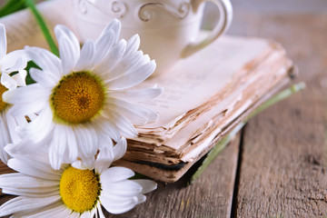 Fototapeta na wymiar Old book with beautiful flowers and cup of tea on wooden table close up