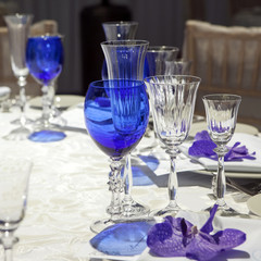serviette on a plate served on the festive table. Blue goblet and violet orchid