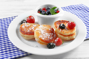 Fritters of cottage cheese with berries in plate on table, closeup