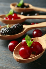 Forest berries in wooden spoons on color background