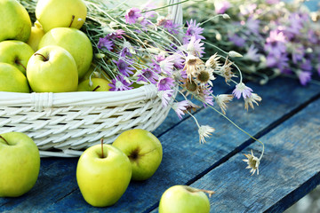 Green apples with bouquet of wildflowers on wooden table, closeup