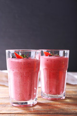 Glasses of berry smoothie on wooden table on dark background