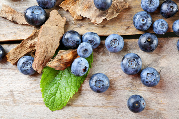Tasty ripe blueberries with green leaves on wooden table close up