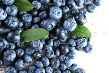 Tasty ripe blueberries with green leaves on wooden table close up