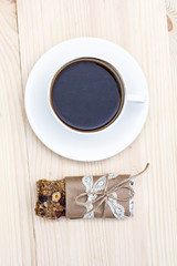 Homemade rustic granola bars with dried fruits and handmade packaged and cup of coffee on wooden background