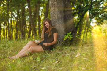 Naklejka na ściany i meble woman girl sits reading a book under a tree in the forest park o