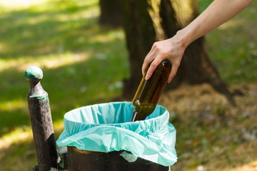Hand of woman throwing glass bottle into recycling bin, littering of environmental