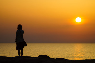 Fototapeta premium Sunset silhouette of young girl waiting for someone on seaside