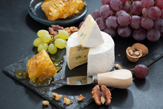 Camembert with fresh honey, grapes and nuts on a dark background