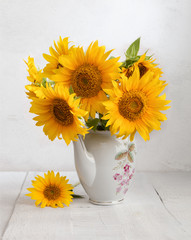 Bouquet of sunflowers in old ceramic jug against a white wooden wall.