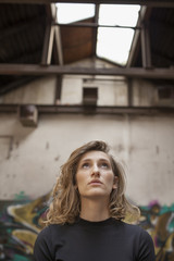 Beautiful woman with a serious expression on her face looking up with a view of abandoned building in the background