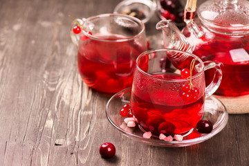 Hot berry tea in glass cups and teapot over rustic wooden background. 
