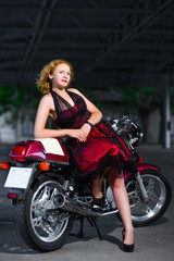 Naklejka na ściany i meble Biker girl in dress on a motorcycle over the background of dark