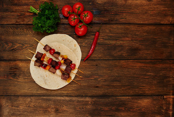 On the table is a plate with slices of bright meat on skewers