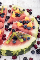 colorful tropical fruit watermelon pizza topped with kiwifruit, blueberries, orange and fresh berries cut into segments on a rustic wooden board