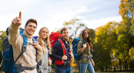 smiling friends with backpacks hiking over nature