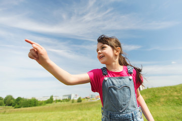 happy little girl pointing finger on summer field