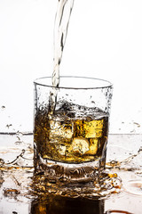 Whisky pouring on ice in glass.
