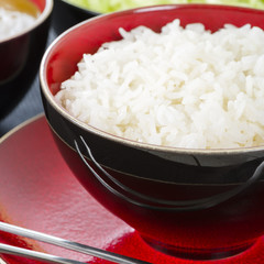 Boiled Rice - Steamed rice in a black and red bowl and metal chopsticks.
