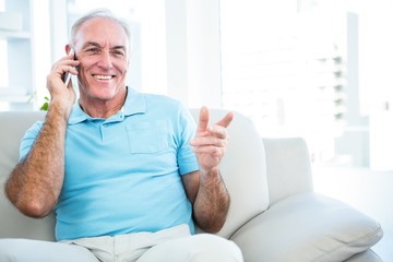 Senior happy man using smartphone while sitting on sofa