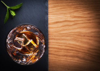 Glass of whiskey with ice on black stone table. Top view with copy space
