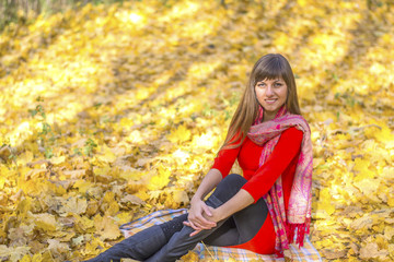 Young cute girl sitting in the Park among the autumn leaves