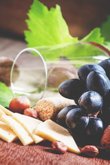 Cheese, blue grapes, vine, nuts and a glass, selective focus