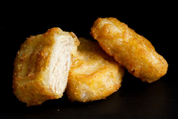 Three golden deep-fried battered chicken nuggets isolated on bla