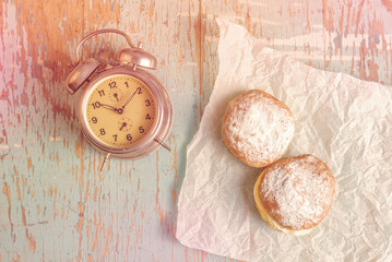 Sweet sugary donuts and vintage clock on rustic table