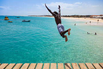 Naklejka premium Teenage Cape verdean boy jumping on the turquoise water of Sant