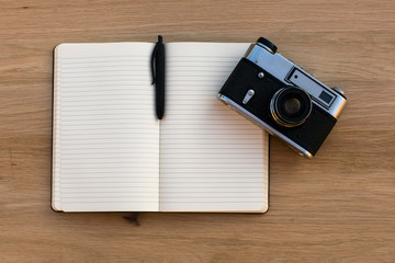 Open notebook with a pen and a vintage film camera, top view on wooden texture of the table.