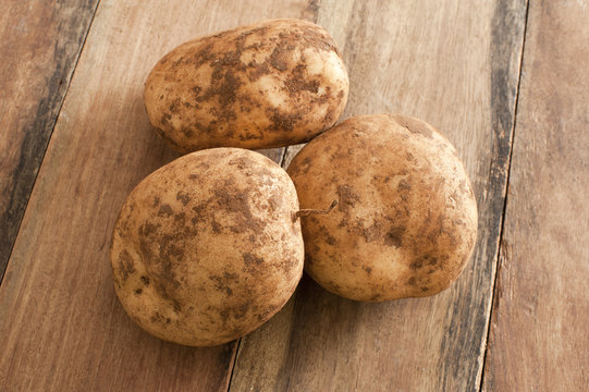 Three Unwashed Potatoes on a Wooden Table