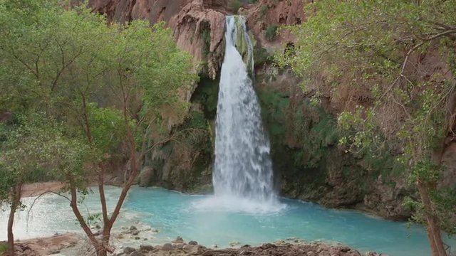 Wide slow motion panning shot of waterfall in rocky landscape / Havasupai, Arizona, United States