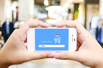 Hand holding smart phone with www. on search bar over blur store